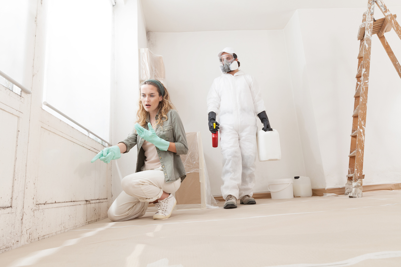 Concerned woman at a home renovation site shows a mold problem to a professional worker using products for mold remediation treatment. Concept cost of mold inspection.